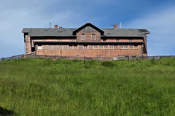 Długi rząd okien przestronnej jadalni w zabytkowym, drewnianym obiekcie górującym nad zielonym zboczem góry